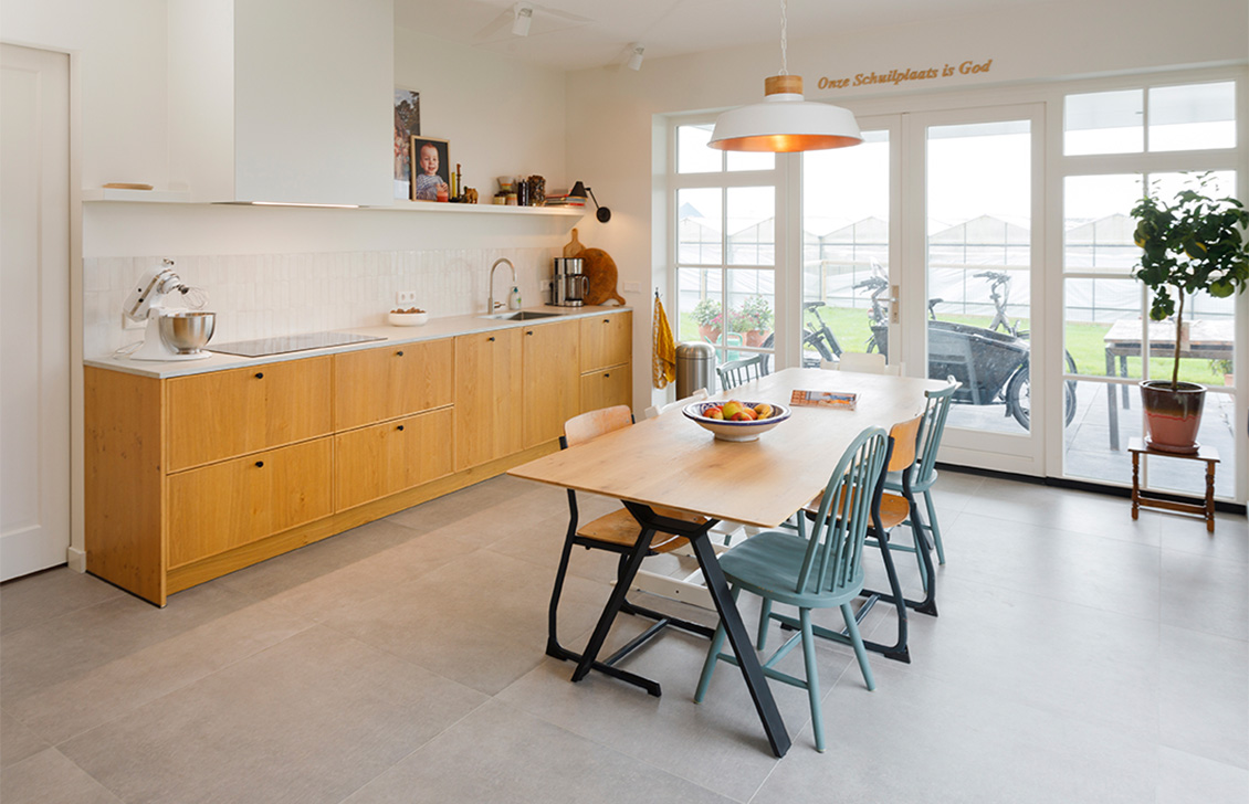 Keuken met houten kastdeuren, wit aanrechtblad, ingebouwde apparatuur, inductiekookplaat en een strakke kraan met spoelbak.