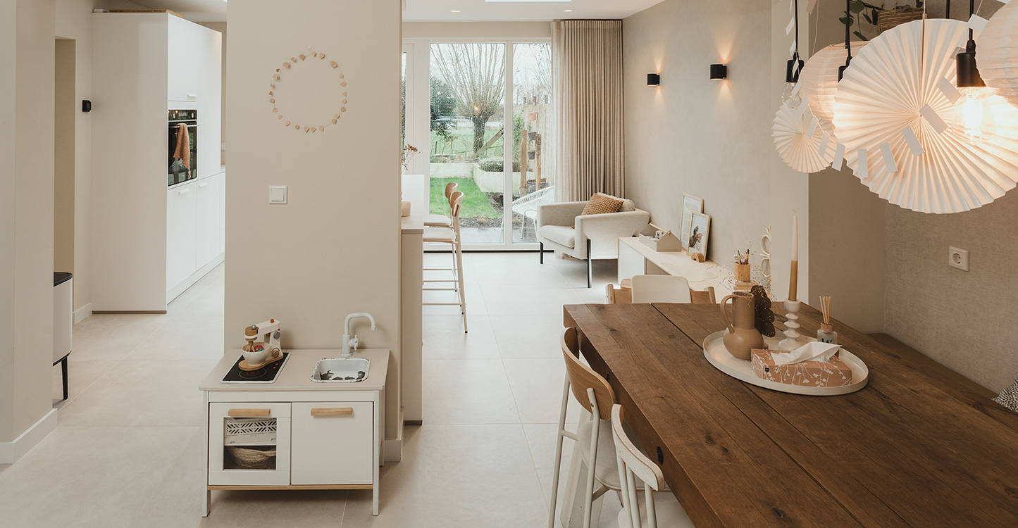 Eethoek, houten tafel, met keuken en zithoek op achtergrond. Voor de muur speelgoed keuken