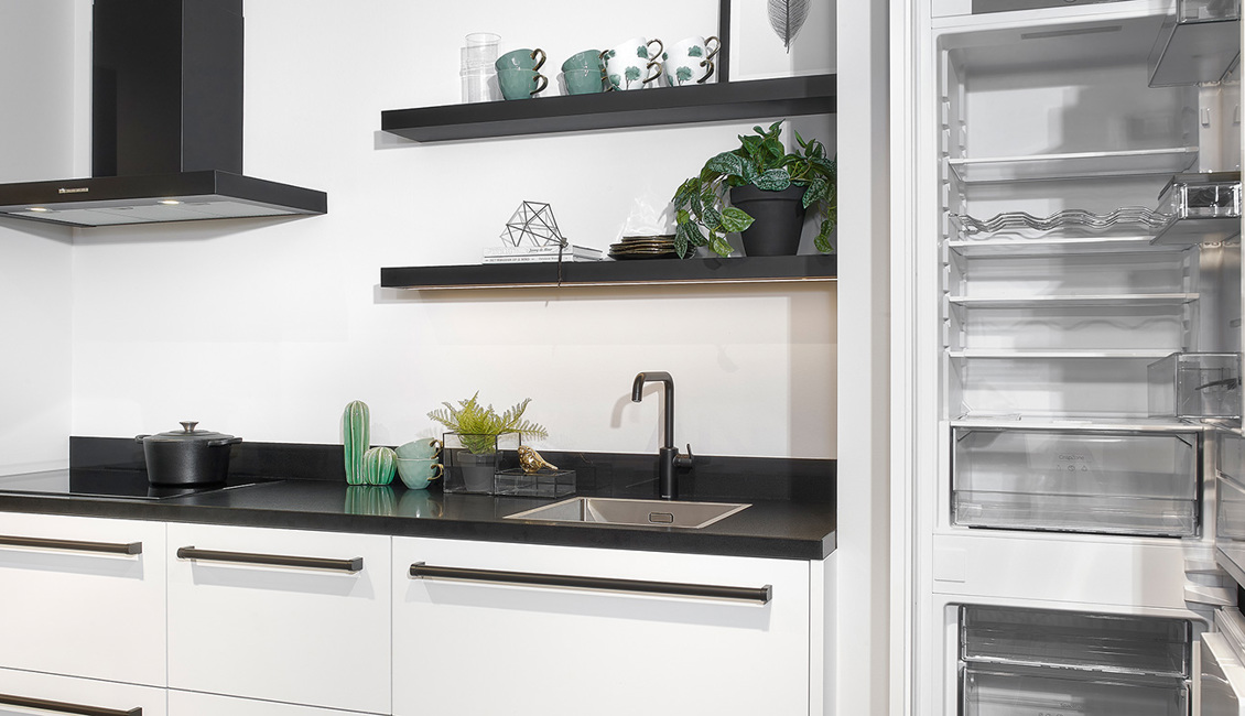 Witte keuken met zwart werkblad en grote koelkast