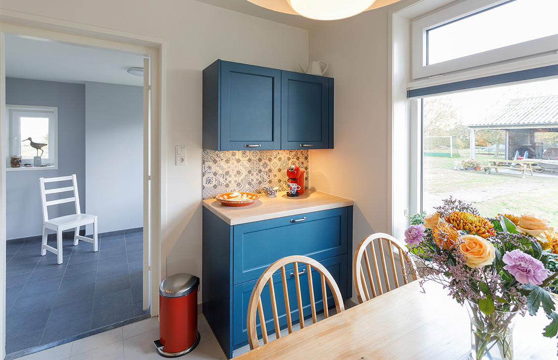 Blauwe keuken met klassieke tegels als achterwand, houten werkblad, moderne apparatuur en decoratieve elementen.