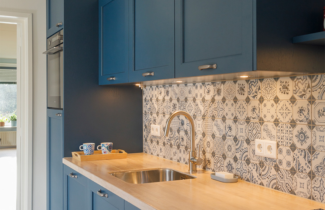 Blauwe keuken met klassieke tegels als achterwand, houten werkblad, moderne apparatuur en decoratieve elementen.