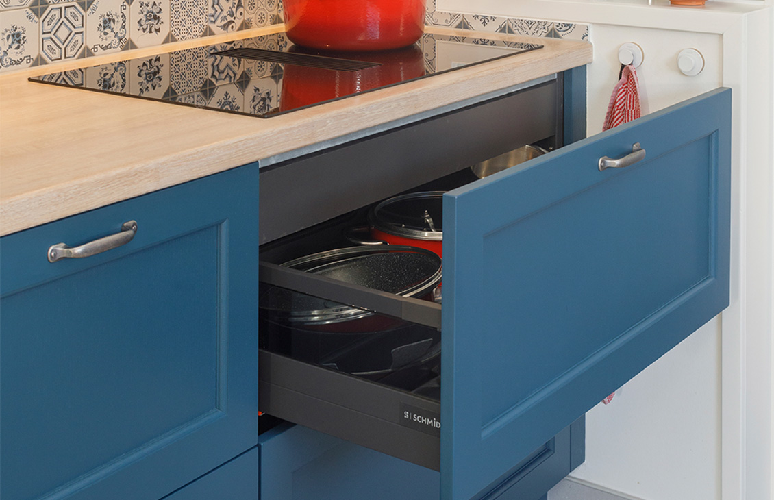 Blauwe keuken met klassieke tegels als achterwand, houten werkblad, moderne apparatuur en decoratieve elementen.