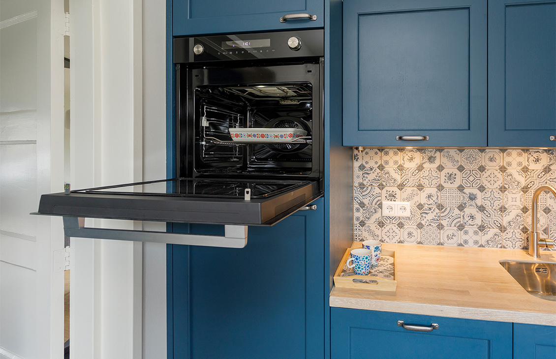 Blauwe keuken met klassieke tegels als achterwand, houten werkblad, moderne apparatuur en decoratieve elementen.